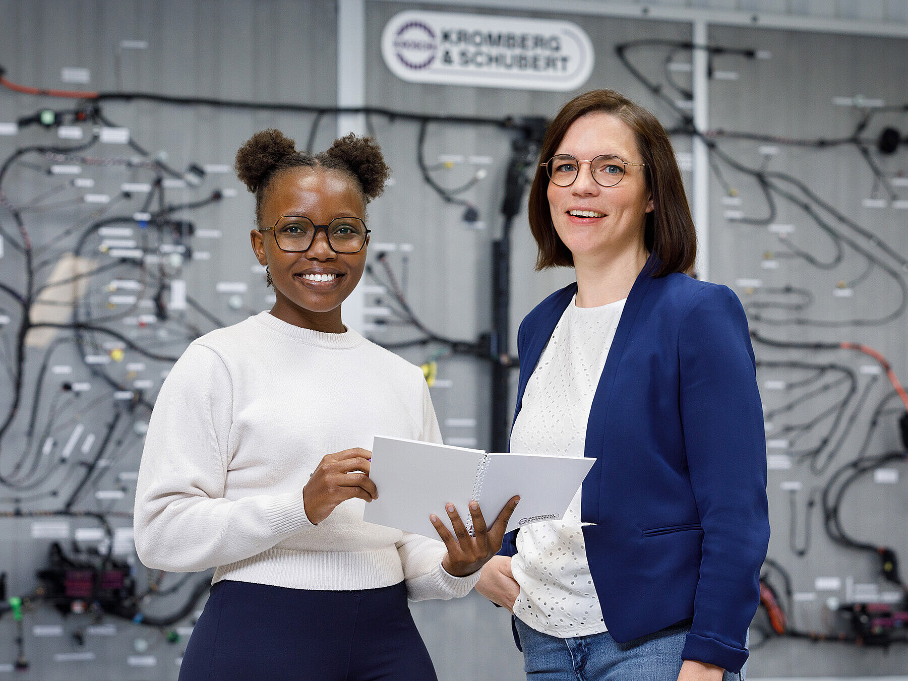 Zwei lachende Mitarbeiterinnen vor einem Bordnetz.
